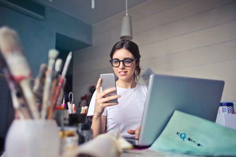 woman in white t shirt holding smartphone in front of laptop